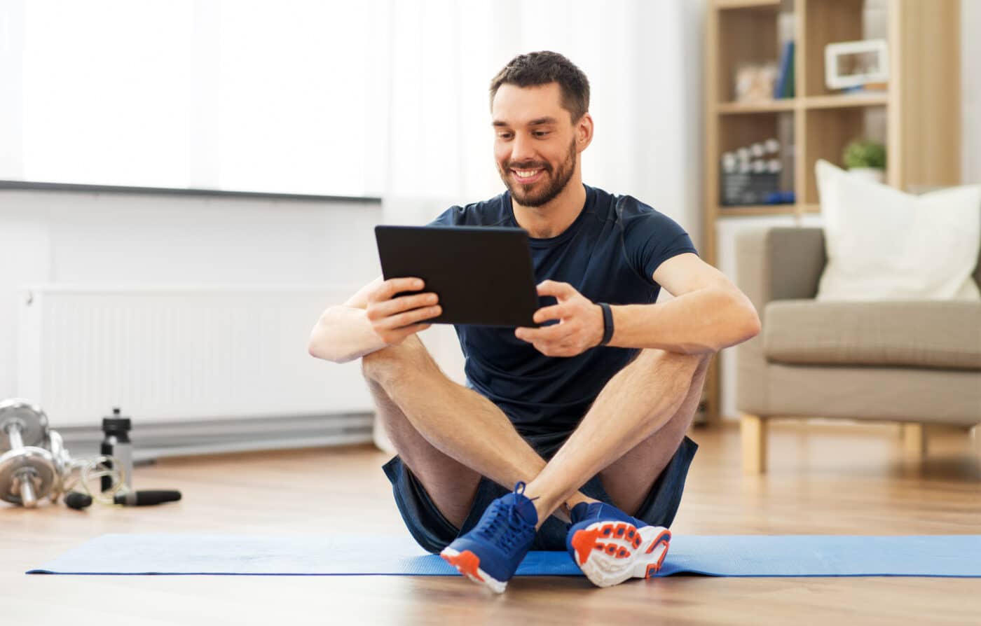 man with tablet computer on exercise mat at home